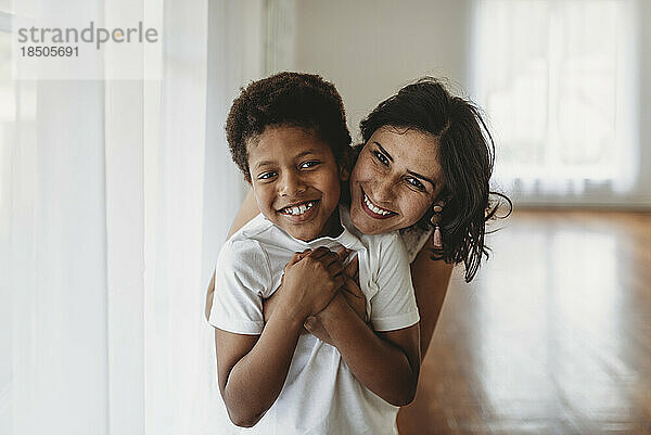 Mutter und Sohn umarmen sich im Studio mit natürlichem Licht und lächeln in die Kamera