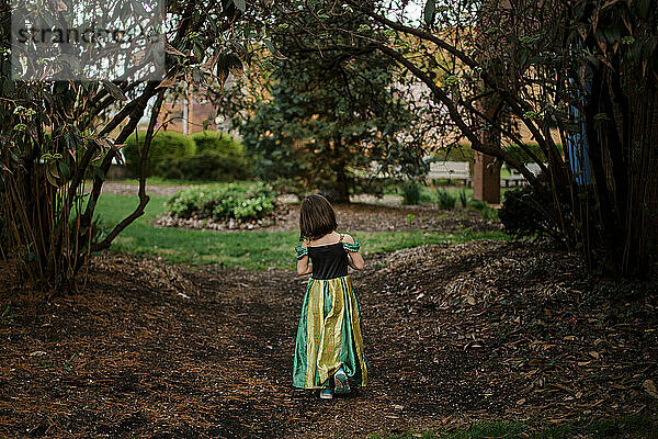 A little girl in a princess costume walks alone on a wooded path