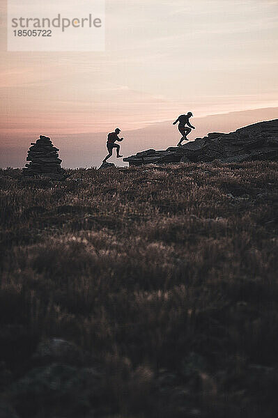 Silhouette männlicher Trailrunner  die bei Sonnenaufgang über den Bergrücken laufen