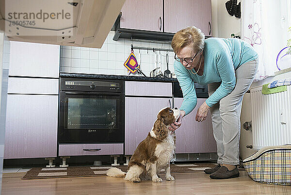 Alte Frau streichelt ihren Hund in der Küche
