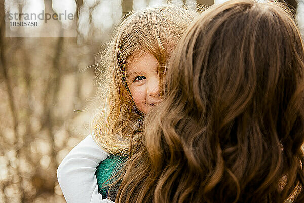 Lächelndes Mädchen blickt draußen im Herbstwald über die Schulter der Mutter