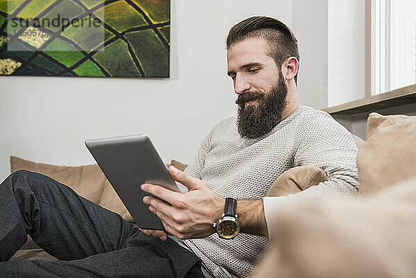 Junger Mann benutzt digitales Tablet auf dem Sofa