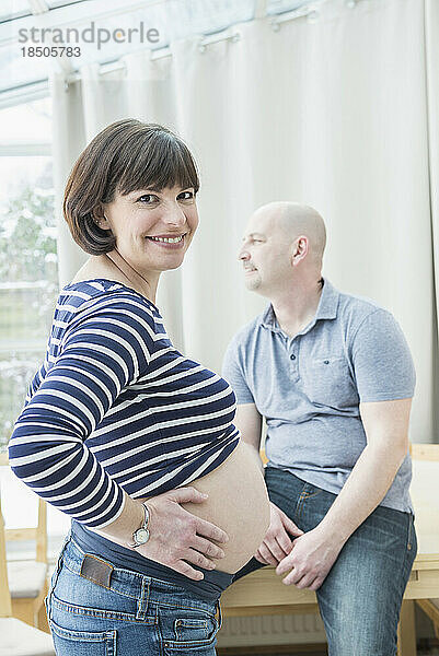 Porträt einer schwangeren Frau mit Ehemann  der am Tisch sitzt