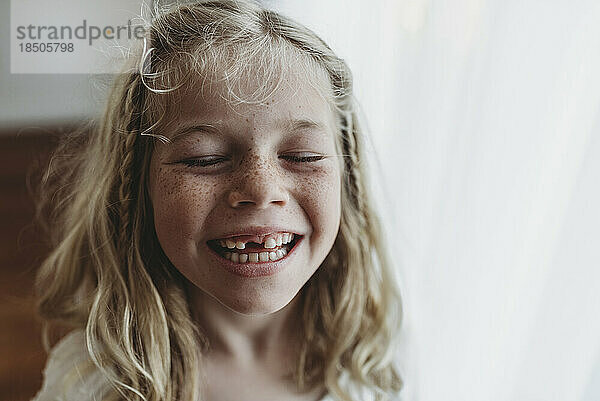 Porträt eines jungen sommersprossigen lächelnden Mädchens  dem Zahn mit geschlossenen Augen fehlt