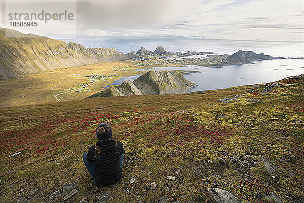 Frau sitzt auf einem Hügel und blickt auf die Bucht in Vaeroy  Lofoten
