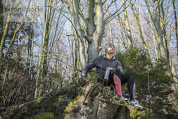 Fitter junger Mann entspannt sich auf Baumstumpf im Wald