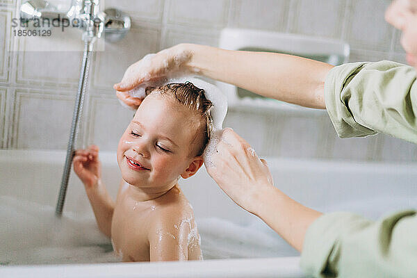 Frau badet ein kleines glückliches Mädchen und wäscht ihr Haar