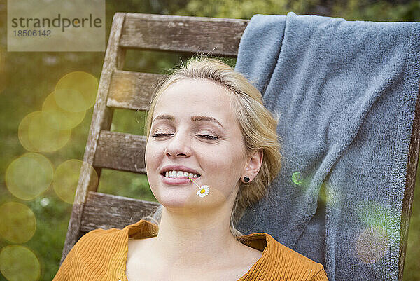 Schöne junge Frau entspannt sich mit einer Blume im Mund im Garten  München  Bayern  Deutschland