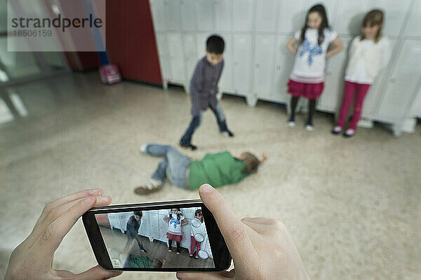 Die Hand einer Person filmt zwei Schüler  die sich im Schulkorridor mit einem Mobiltelefon streiten  Bayern  Deutschland