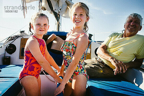 Junge Mädchen lachen und lächeln mit Opa in Badeanzügen auf einem Segelboot