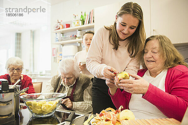 Ältere Frau mit Mädchen schneidet Apfel im Pflegeheim