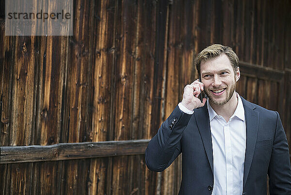 Mittlerer erwachsener Geschäftsmann  der draußen mit dem Handy telefoniert und lächelt  Bayern  Deutschland