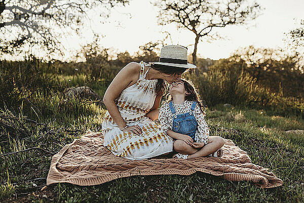 Mutter und Tochter sitzen auf einer Decke im Feld und küssen sich