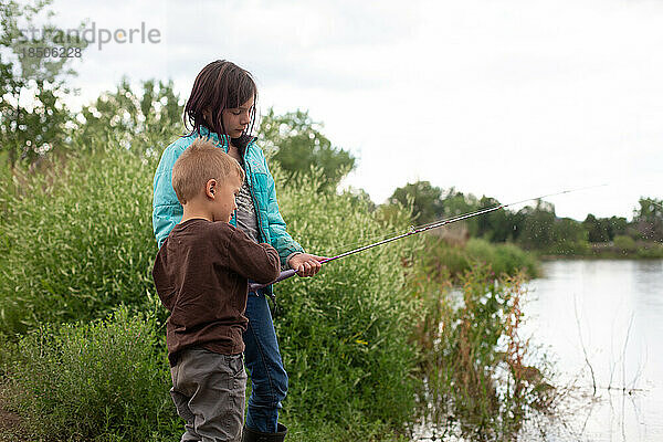 Geschwister angeln an einem Teich  Schwester hilft kleinem Bruder