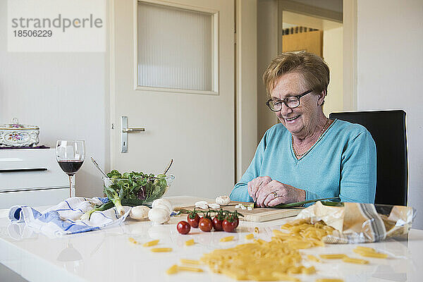 Alte Frau schneidet Frühlingszwiebeln am Küchentisch