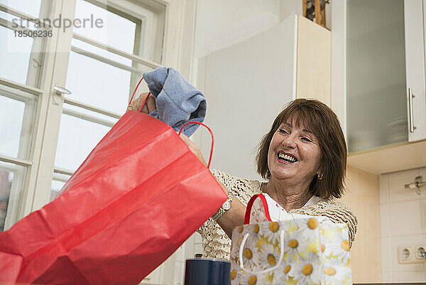 Ältere Frau schaut in die Einkaufstasche und lächelt in der Küche  München  Bayern  Deutschland