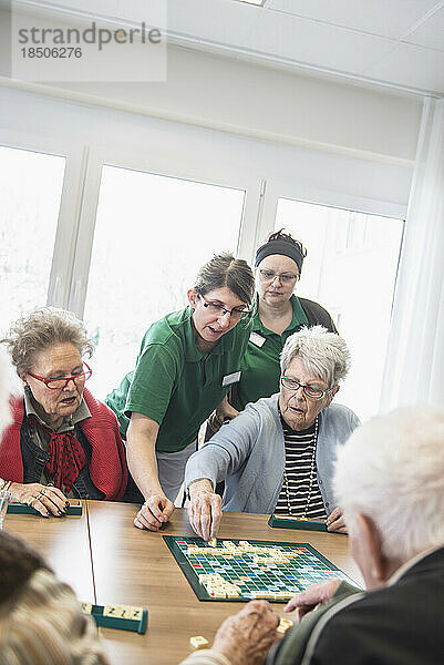 Senioren spielen Brettspiel mit Krankenschwester im Pflegeheim