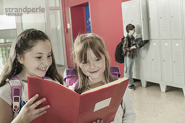 Zwei Schulmädchen lesen ein Buch im Flur in der Nähe von Schließfächern  Bayern  Deutschland