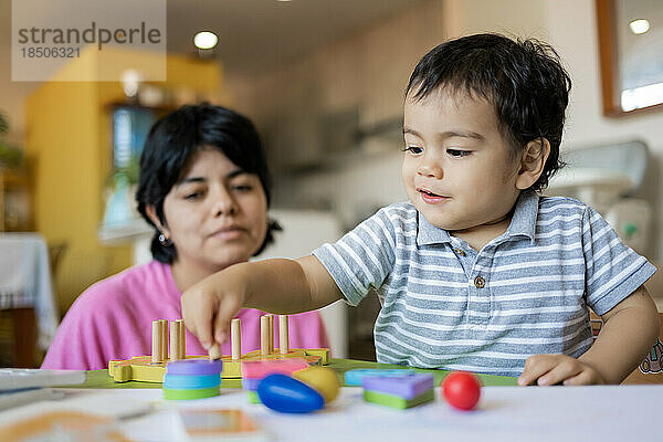 Lateinische Mutter und kleiner Sohn spielen zusammen mit hölzernen Logikspielzeugen.
