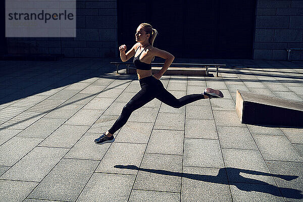 Blonde  fitte Frau in schwarzer Sportbekleidung läuft während des Trainings im Freien