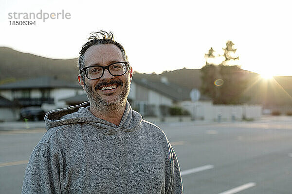 Mann mittleren Alters mit Brille lächelt draußen bei Sonnenuntergang