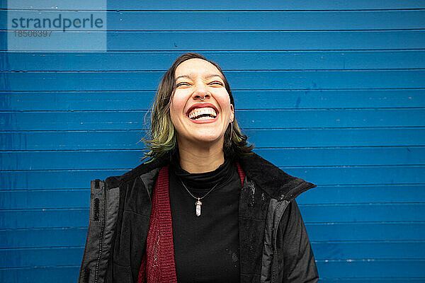 Lachende junge Frau mit geschlossenen Augen auf blauer Wand  im Regen.