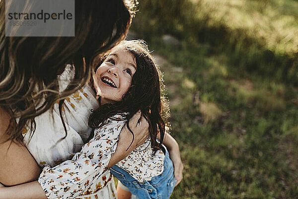 Junge glückliche Tochter lacht  während sie draußen von der Mutter umarmt wird