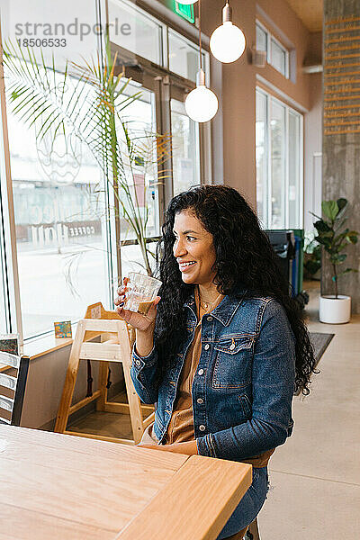 Glückliche Latina-Frau lächelt und hält Kaffee im Café