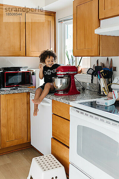 Biracial-Junge  Kleinkind sitzt auf der Küchentheke und backt Kekse