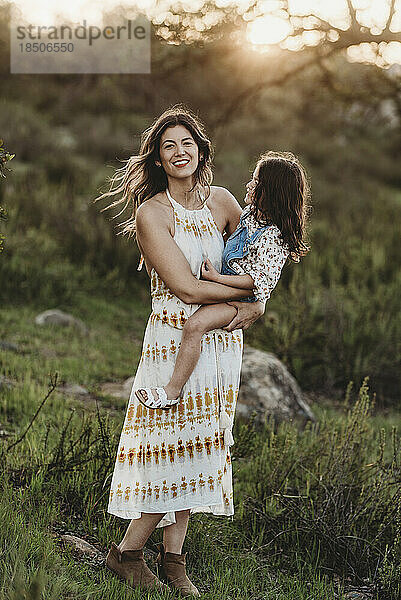 Ganzkörperansicht von Mutter und Tochter  die sich auf einem sonnigen Feld umarmen