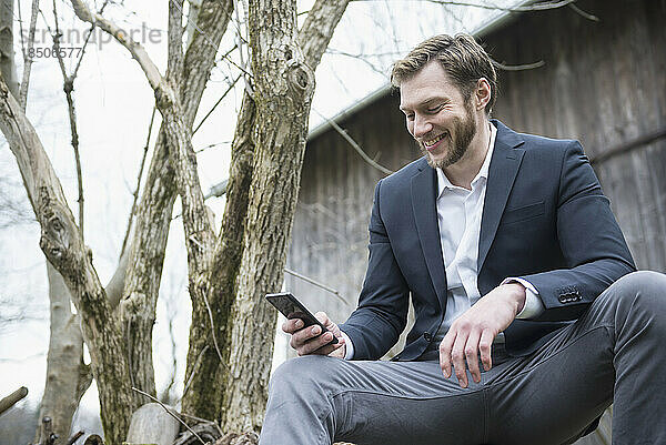 Mittlerer erwachsener Geschäftsmann  der draußen sein Mobiltelefon benutzt und lächelt  Bayern  Deutschland