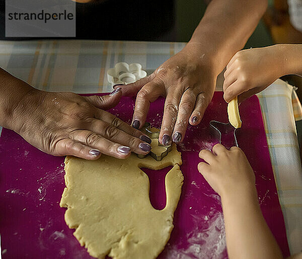 Hände einer erwachsenen Frau und eines Kindes  die Kekse ausschneiden