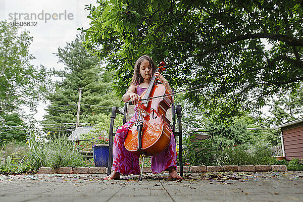 Ein kleines Kind spielt barfuß Cello im Garten auf der Terrasse