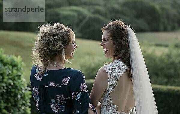 Braut und ihre Freundin halten Händchen und lachen an ihrem Hochzeitstag