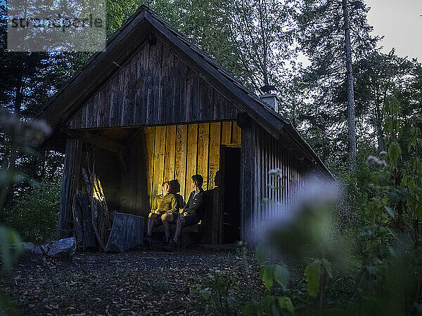 Zwei männliche Wanderer entspannen sich nachts vor einer kleinen Hütte im Schwarzwald  Baden-Württemberg  Deutschland