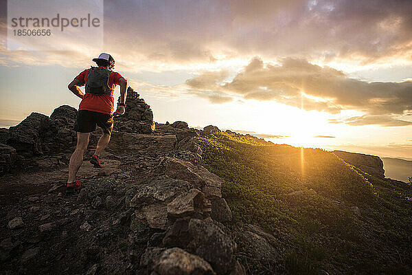 Trailrunning-Mann läuft bei Sonnenaufgang mit Steinhaufen aus niedrigem Winkel