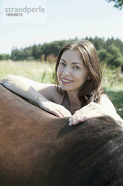 Porträt einer reifen Frau  die sich auf den Rücken ihres braunen Pferdes stützt und lächelt  Bayern  Deutschland