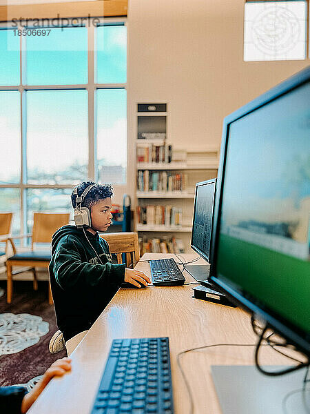 Kind gemischter Abstammung konzentriert sich auf den Computerbildschirm in der Bibliothek