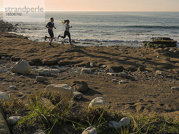 Mann und Frau laufen auf einem Singletrail am Strand von Azkorri