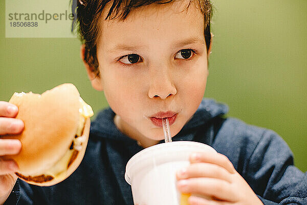 Junge isst und trinkt vor grünem Hintergrund