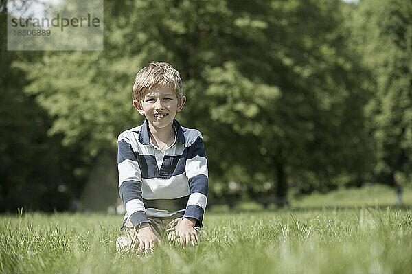 Junge lächelt und sitzt auf einem Feld im Park  München  Bayern  Deutschland