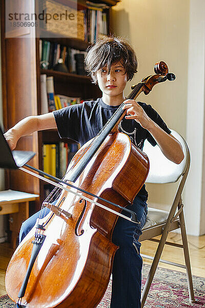 Ein konzentrierter Junge sitzt im Fensterlicht und übt Cello
