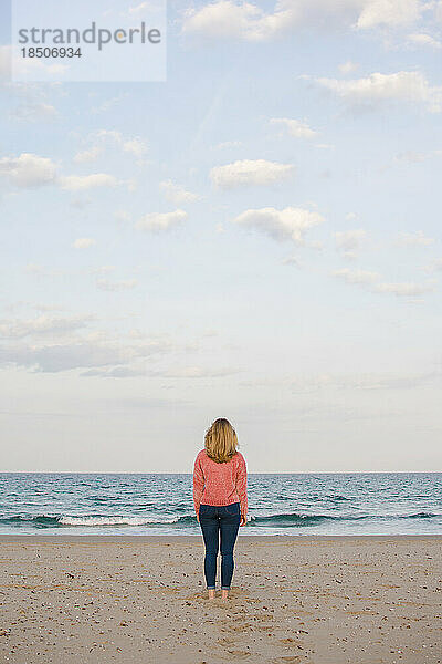 Junge Frau geht an der Küste entlang und beobachtet das Meer