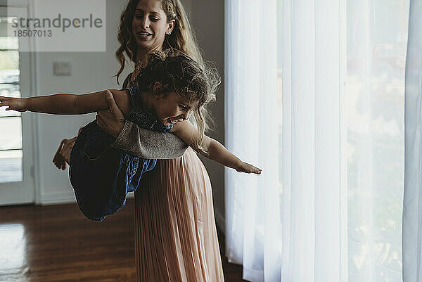 Daughter and mother playing airplane in natural light studio