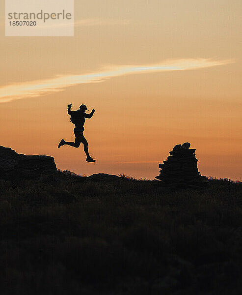 Silhouette eines männlichen Trailrunners  der bei Sonnenaufgang vom Felsen springt