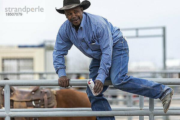 Ein Cowboy hüpft beim Az Black Rodeo mit einer Dose Bier über einen Zaun