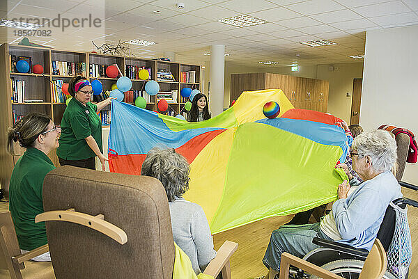 Pflegepersonal mit Mädchen und älteren Frauen bei sportlichen Übungen mit Fallschirm und Ball im Pflegeheim