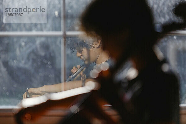 Spiegelbild eines Jungen  der Cello übt  im Fenster