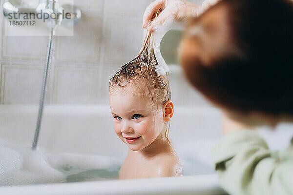 Frau badet ein kleines glückliches Mädchen und wäscht ihr Haar