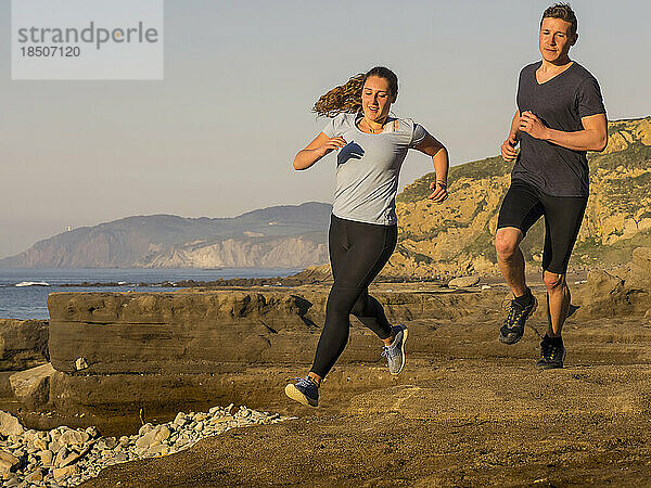 Mann und Frau laufen auf einem Singletrail am Strand von Azkorri